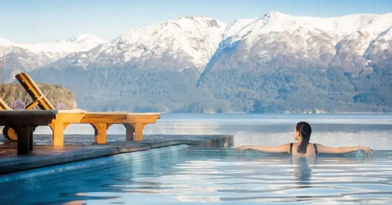 Persona nadando en piscina azul frente a montañas nevadas y bosque