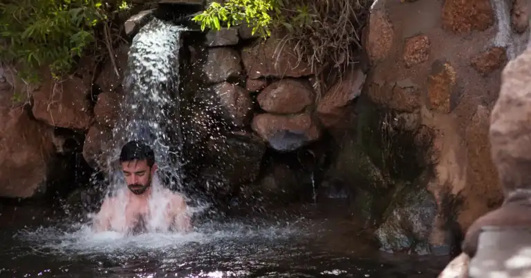 Persona disfruta de baños termales en aguas turquesas dentro de roca roja
