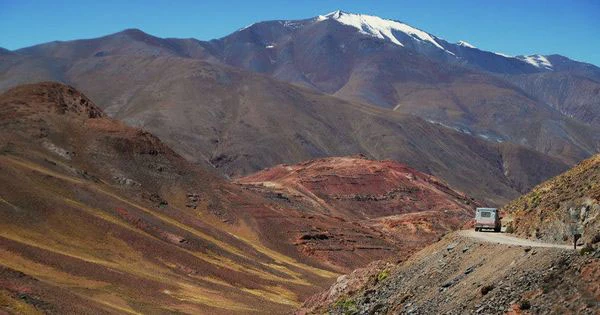 Montaña con nieve en altitud en cordillera desértica con camino y vehículo