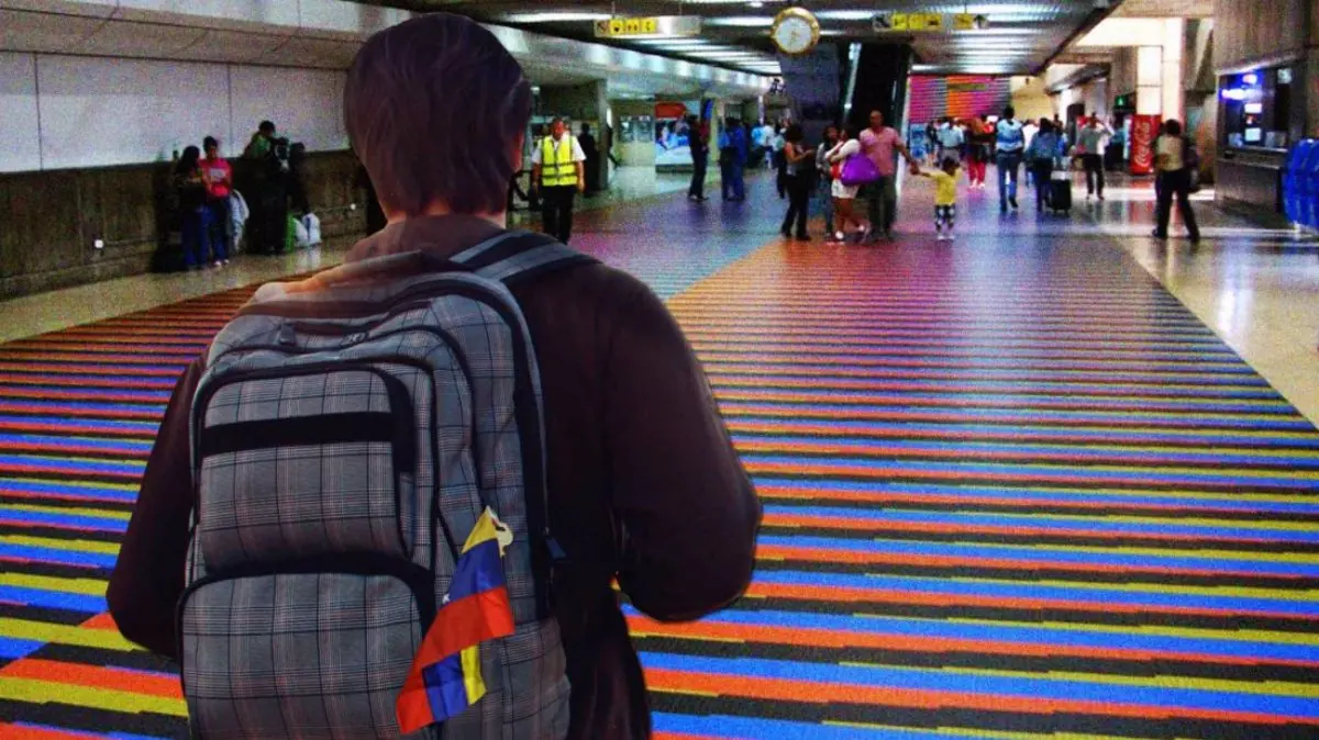 Viajero con mochila de espaldas en un corredor con piso de rayas de colores arco iris