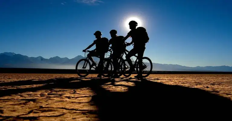 Tres personas en bicicletas silueteadas contra montañas y cielo azul