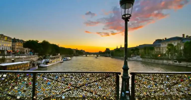 Puente peatonal sobre el río al atardecer con barandilla cubierta de candados de metal