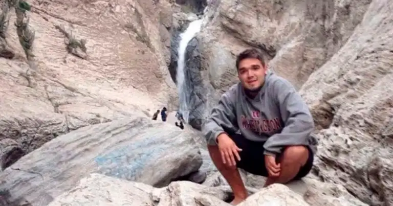 Joven hombre junto a una cascada en desfiladero de rocas grises