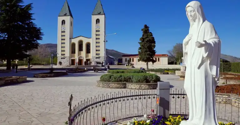 Estatua blanca de Virgen María ante iglesia moderna con cruz