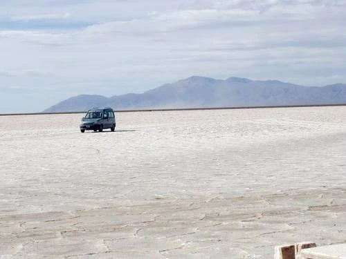 Vehículo 4x4 en llanura blanca de sal mineral con montañas de fondo