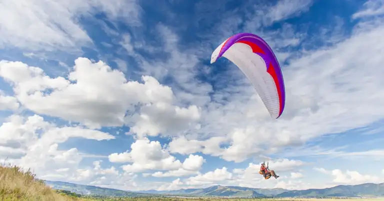 Paracaidista con parapente rojo y blanco sobre paisaje de montañas verdes