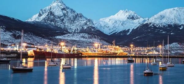 Ushuaia iluminada al atardecer con montañas nevadas reflejadas en aguas tranquilas