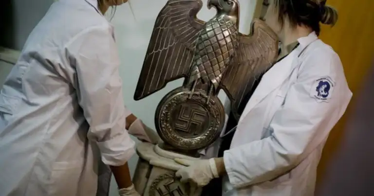 Dos personas sostienen emblema de águila de metal