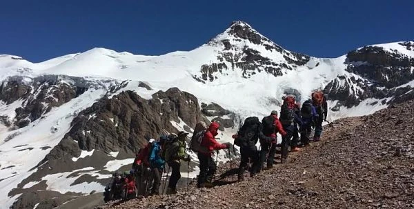 Grupo de montañeros en ladera rocosa con montaña nevada al fondo
