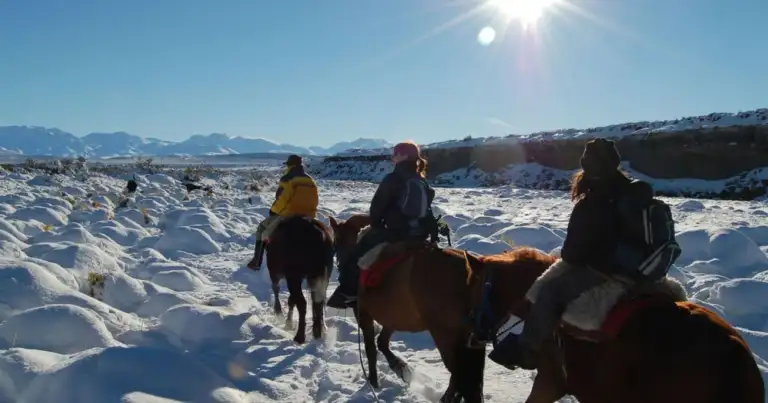 Tres jinetes a caballo en paisaje nevado con montañas al fondo