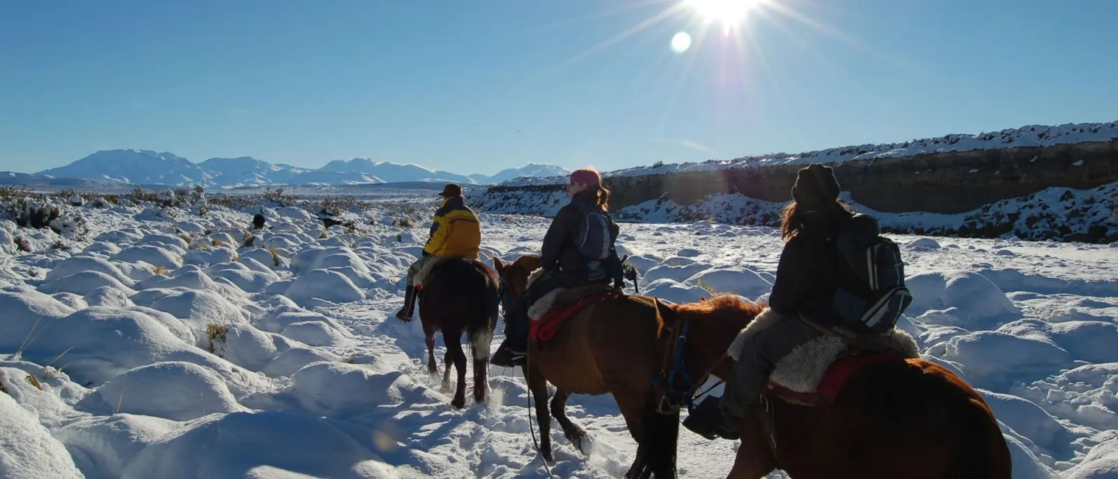 Tres jinetes a caballo en paisaje nevado con montañas al fondo