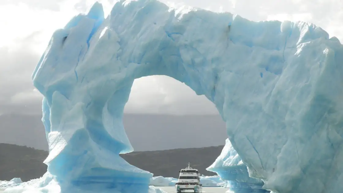 Enorme glaciar azul en forma de arco sobre embarcación turística en el agua