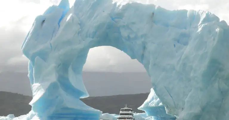 Enorme glaciar azul en forma de arco sobre embarcación turística en el agua