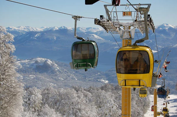 Dos cabinas de telesilla verde y amarilla con montañas nevadas de fondo