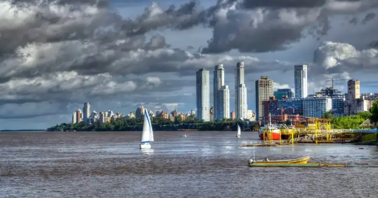 Río urbano con rascacielos y embarcación de vela blanca