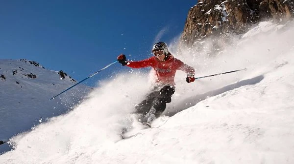 Esquiador descendiendo pendiente de nieve profunda con montaña al fondo