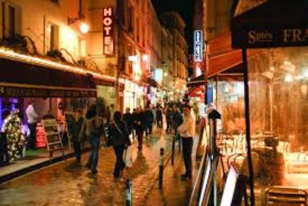 Calle del Barrio Latino de París iluminada de noche con tiendas y peatones