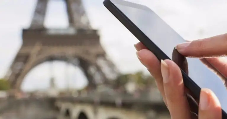 Mano sosteniendo teléfono con Torre Eiffel borrosa de fondo