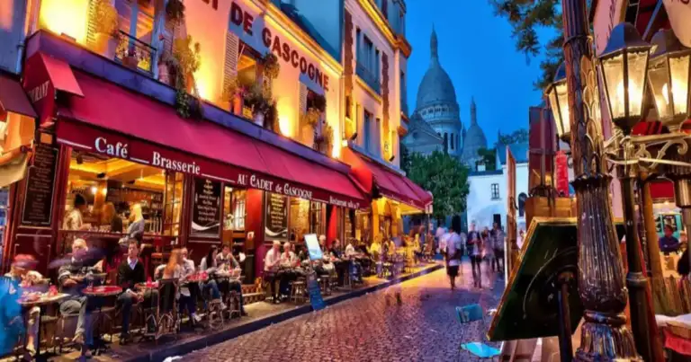 Calle con cafeterías iluminadas y personas al atardecer