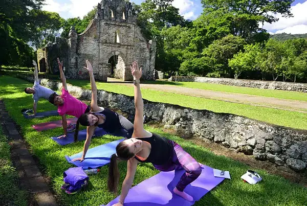 Grupo practicando yoga en hierba con ruinas de piedra al fondo