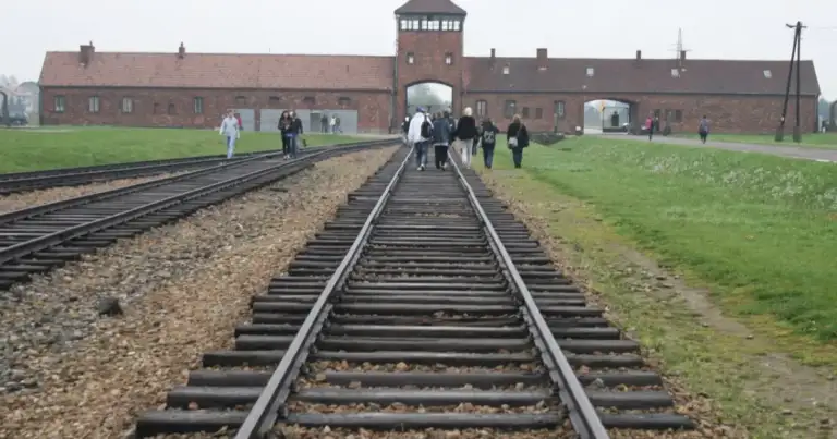 Vías del tren que llegan a la puerta principal de Auschwitz II-Birkenau, con visitantes caminando junto a ellas