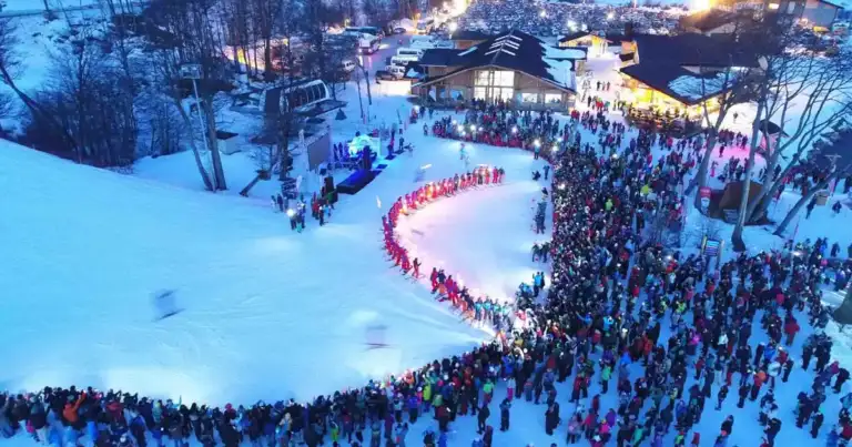 Multitud de personas en la nieve sosteniendo antorchas formando letras al atardecer
