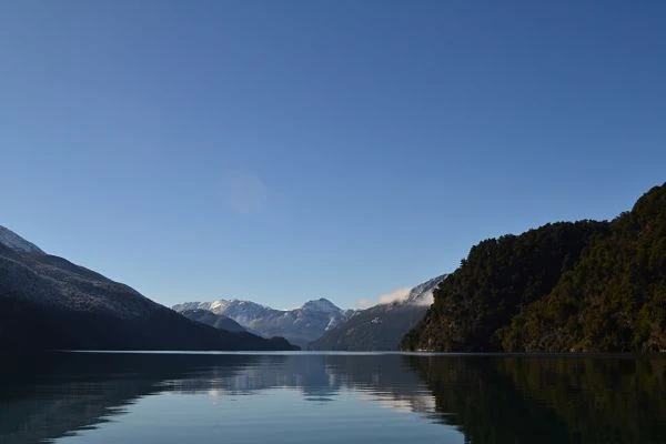 Lago tranquilo con montañas nevadas al fondo rodeado de bosque