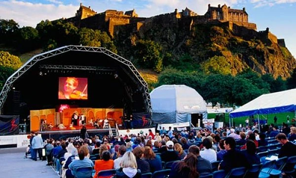 Escenario de concierto iluminado con castillo al fondo
