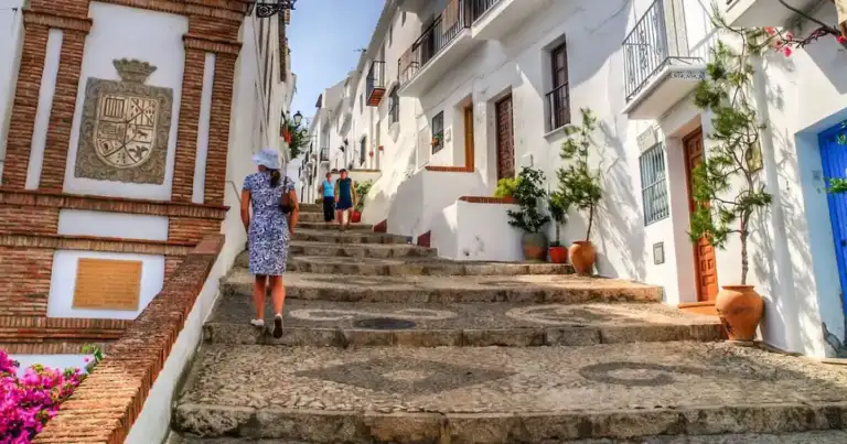 Calle empedrada con casas blancas adornadas con flores rosas en pueblo andaluz