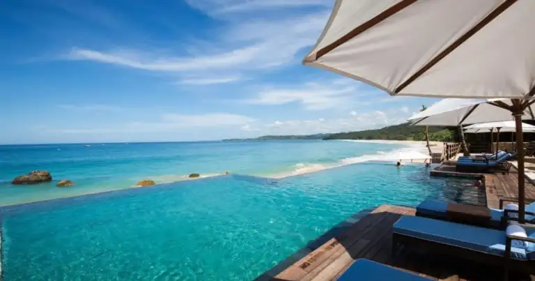 Resort tropical con sombrilla blanca en una playa de agua turquesa cristalina