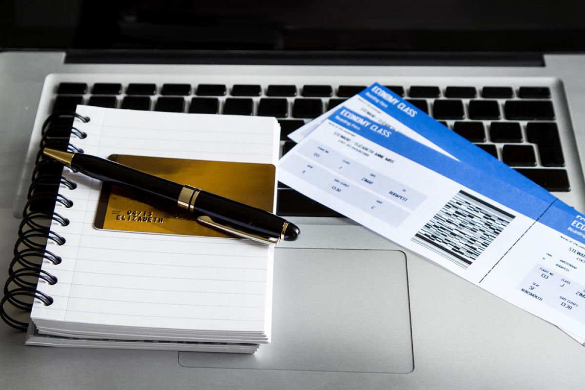 Una laptop para buscar vuelos o alojamientos en sitios web de viajes,con libreta, lapicera y tkt aereos.