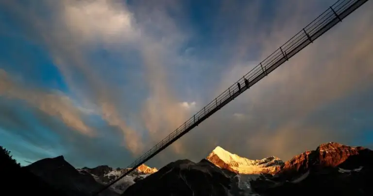 Puente colgante peatonal sobre montañas nevadas al atardecer