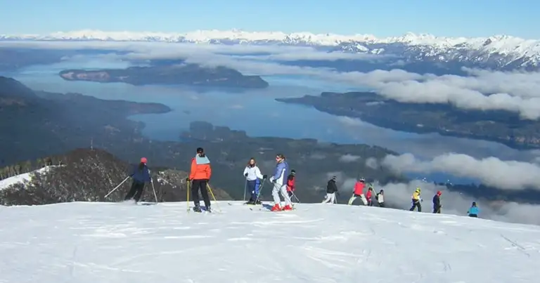 Esquiadores en una pista nevada con vistas a lagos y montañas al fondo