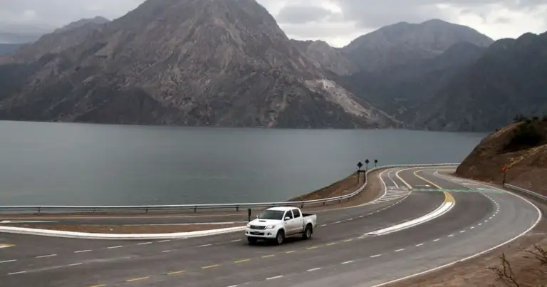 Auto en carretera sinuosa junto a montañas y lago