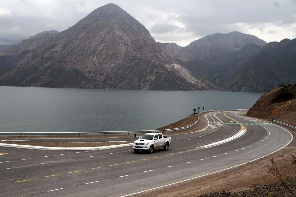Auto en carretera sinuosa junto a montañas y lago