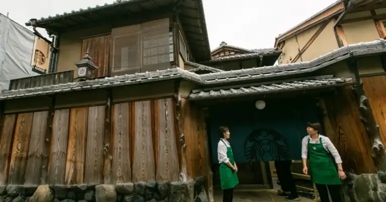 Dos empleados de Starbucks en la puerta de una sucursal con arquitectura tradicional japonesa