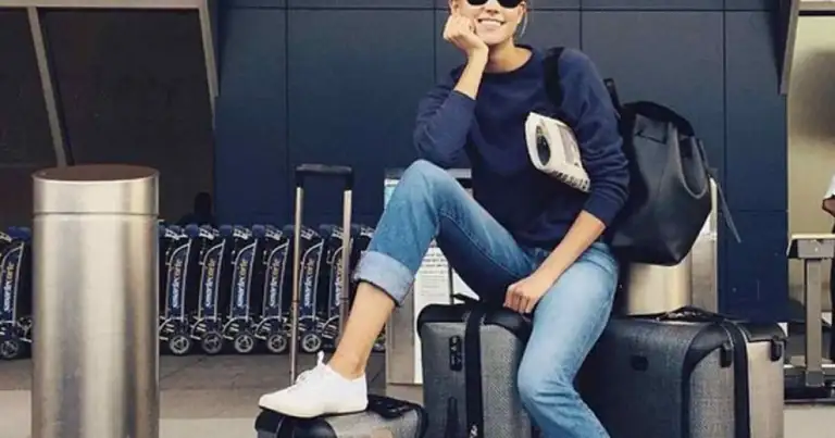 Mujer con gafas de sol y suéter azul oscuro posando con una maleta