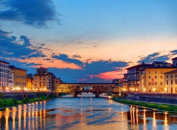 Río Arno con puentes iluminados y edificios renacentistas al atardecer