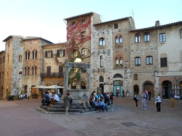 Plaza medieval italiana con pozo, edificios de piedra y torres