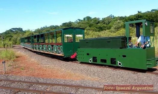 Tren turístico verde en vías de ferrocarril de tierra roja