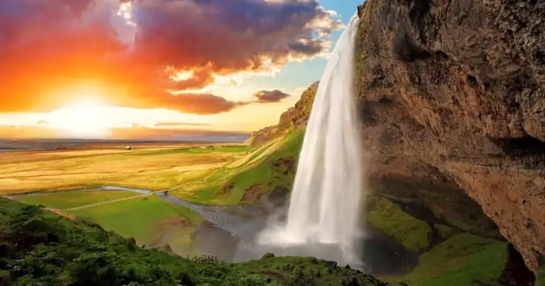 Cascada sobre acantilado rocoso al atardecer con vegetación verde en Islandia