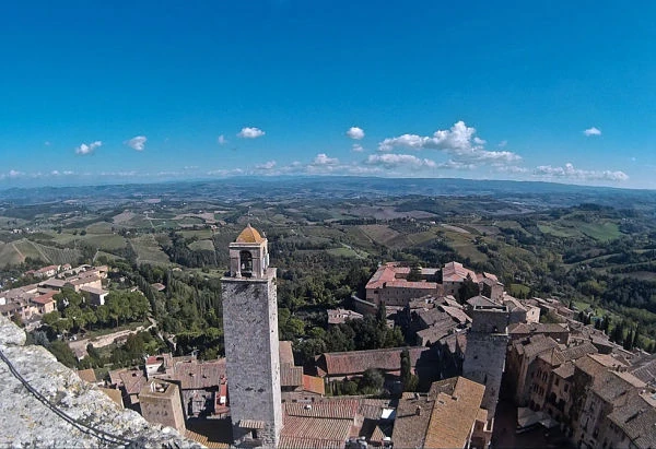 Vista panorámica de pueblo medieval con torres rojas y paisaje toscano