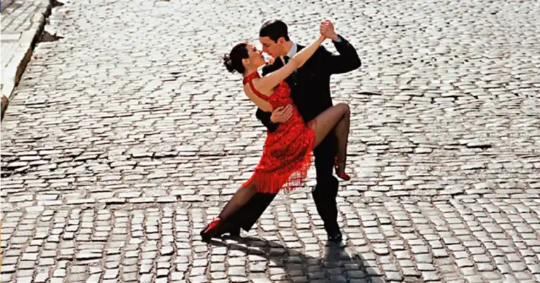 Pareja bailando tango en calle empedrada, mujer en vestido rojo