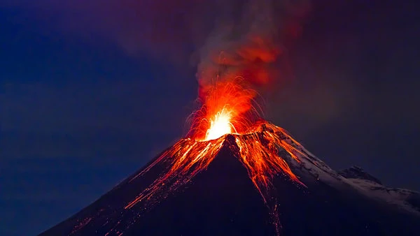 Volcán en erupción con lava roja y naranja en la cima contra cielo oscuro