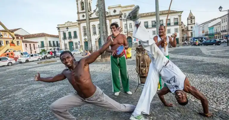 dos hombres de piel negra bailan en una plaza de bahía y una mujer con pantalón verde observa