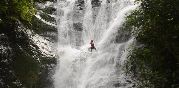 Persona en ropa roja bajo poderosa cascada de agua blanca en paisaje tropical, Costa Rica