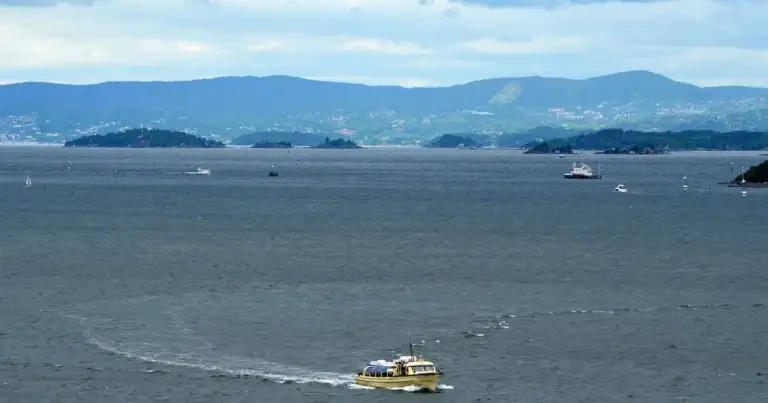 Transbordador amarillo navegando bahía con montañas de fondo