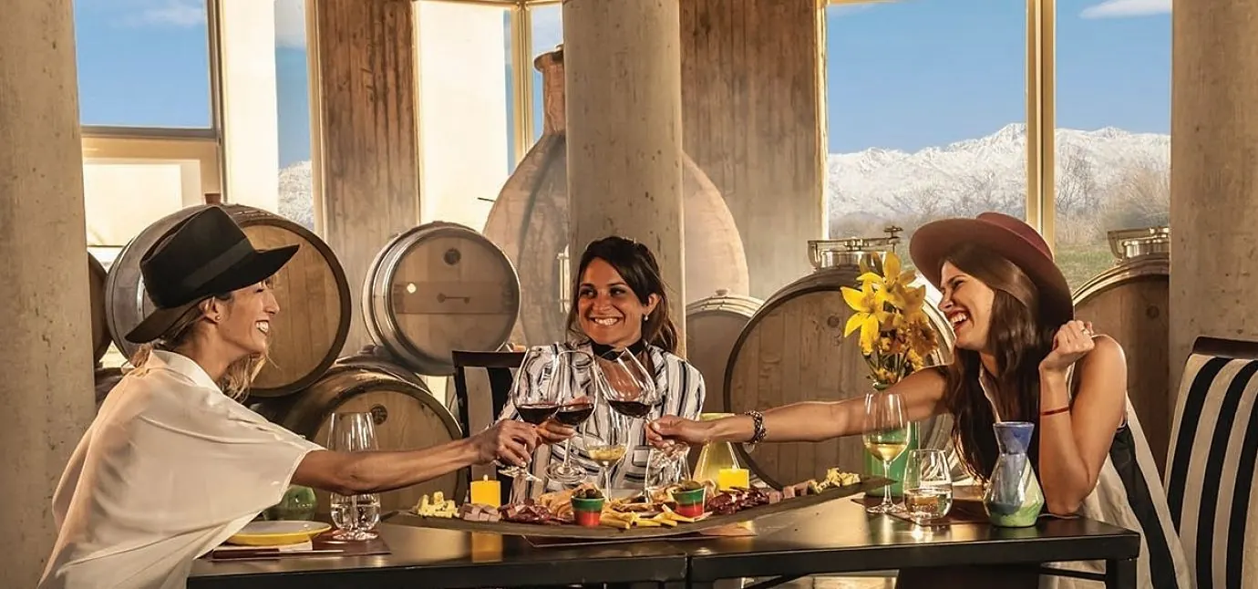 Tres personas brindando en terraza de bodega con montañas nevadas visibles