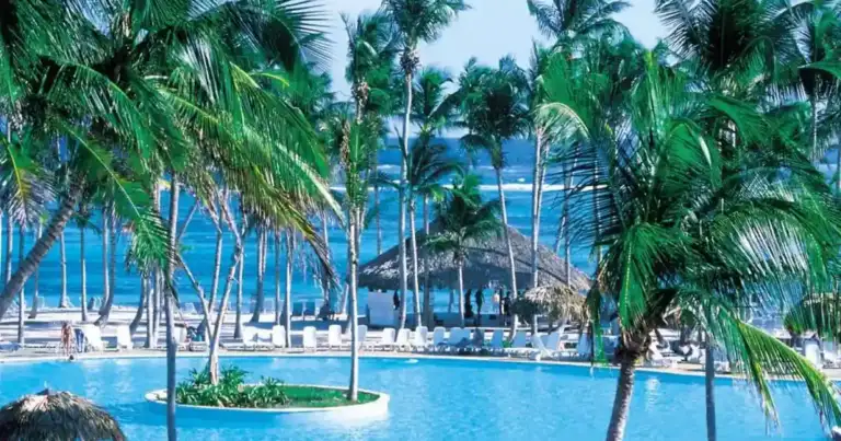 Piscina turquesa de resort con palmeras y sombrillas de playa