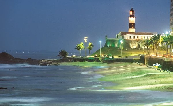 Faro iluminado de noche en costa con playa, agua y arquitectura histórica